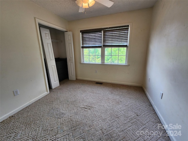 unfurnished bedroom featuring a closet, a textured ceiling, carpet floors, and ceiling fan