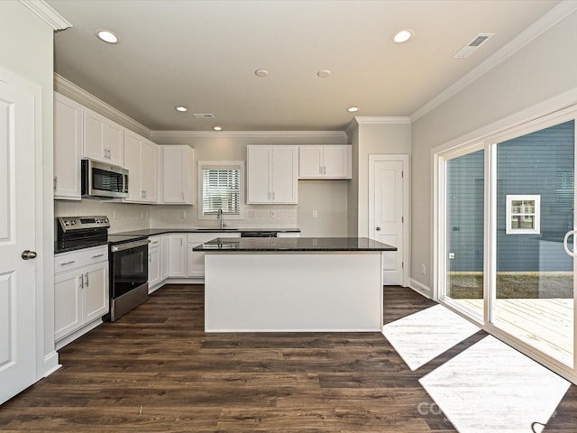 kitchen featuring dark countertops, appliances with stainless steel finishes, white cabinetry, a kitchen island, and a sink