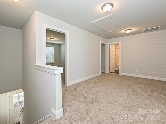 unfurnished room with light carpet, visible vents, attic access, and baseboards