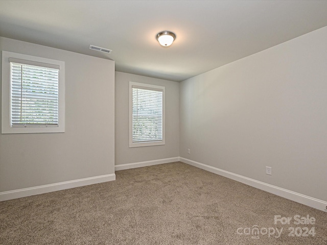 empty room with carpet flooring, visible vents, and baseboards