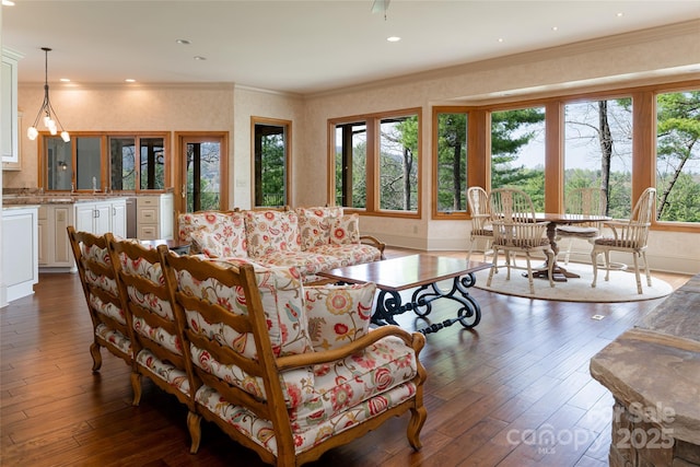 living room with dark wood-type flooring, ornamental molding, and a notable chandelier