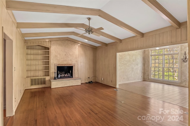 unfurnished living room featuring lofted ceiling with beams, a fireplace, wooden walls, and built in shelves