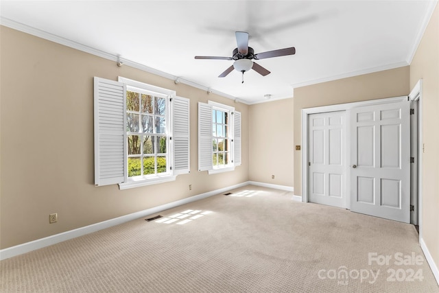 unfurnished bedroom featuring ceiling fan, crown molding, a closet, and light colored carpet