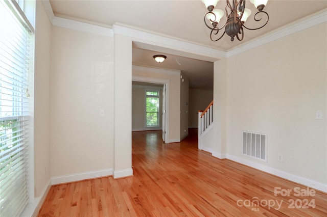 empty room featuring hardwood / wood-style flooring, ornamental molding, and a chandelier