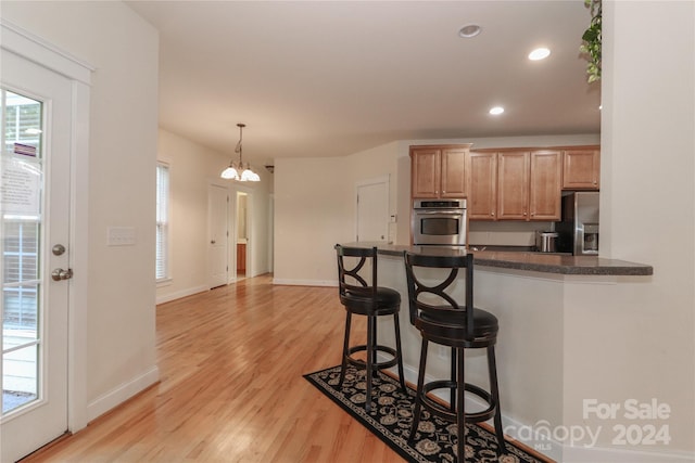 kitchen with a breakfast bar area, hanging light fixtures, kitchen peninsula, stainless steel appliances, and light wood-type flooring