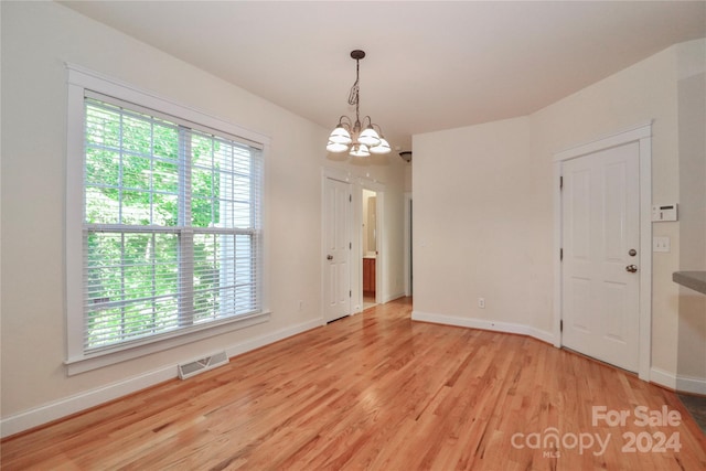 unfurnished room featuring an inviting chandelier and light hardwood / wood-style flooring