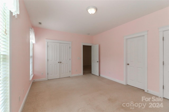 unfurnished bedroom with light colored carpet and a closet