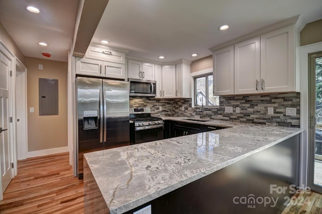 kitchen featuring sink, backsplash, white cabinetry, stainless steel appliances, and light hardwood / wood-style flooring