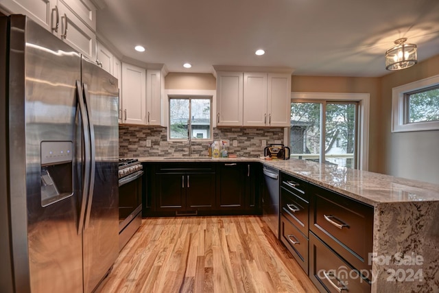 kitchen with white cabinets, backsplash, appliances with stainless steel finishes, sink, and light hardwood / wood-style floors