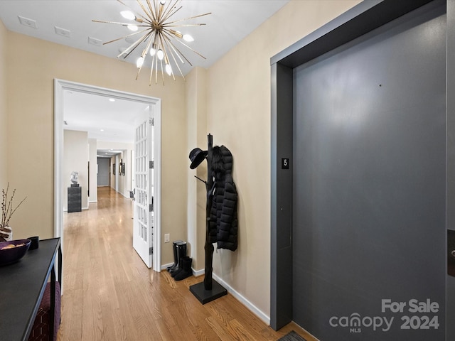 hallway featuring light wood-type flooring, a chandelier, and elevator