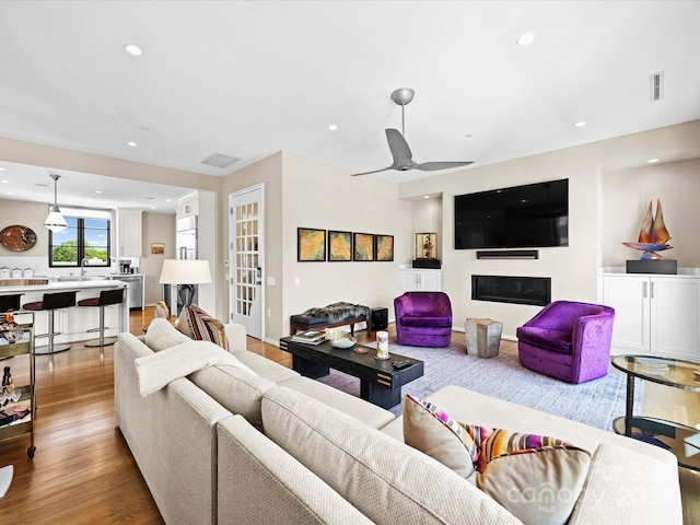 living room featuring ceiling fan, sink, and light wood-type flooring