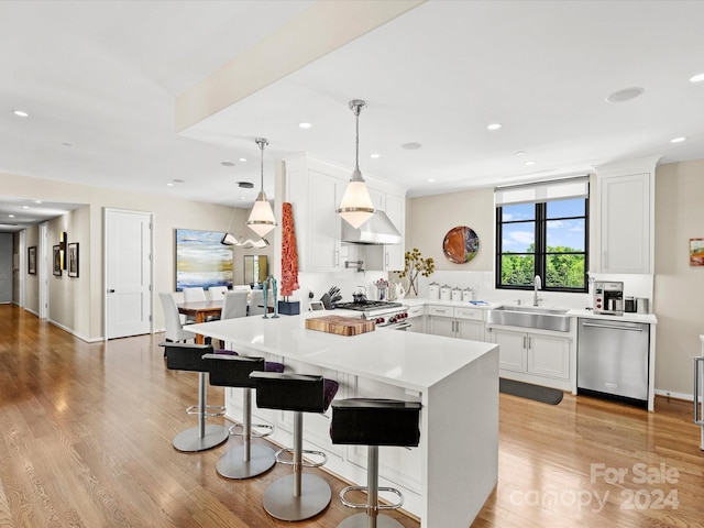 kitchen with appliances with stainless steel finishes, light hardwood / wood-style floors, white cabinetry, sink, and pendant lighting