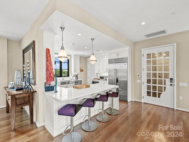 kitchen featuring pendant lighting, a breakfast bar, white cabinets, light wood-type flooring, and built in fridge