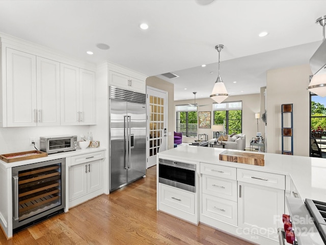 kitchen featuring wine cooler, hanging light fixtures, white cabinets, light wood-type flooring, and stainless steel appliances