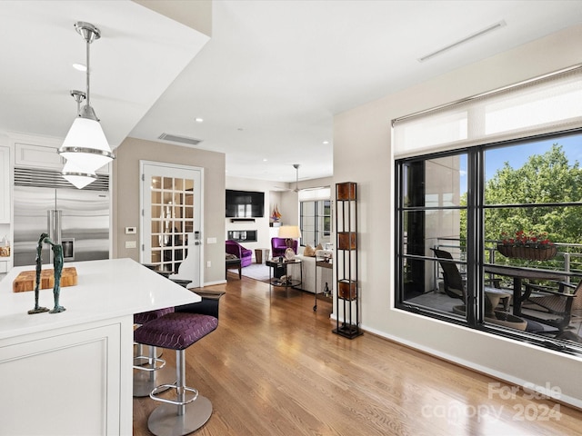 kitchen with white cabinets, decorative light fixtures, built in fridge, light hardwood / wood-style flooring, and a kitchen breakfast bar