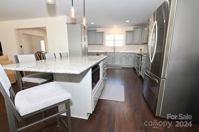 kitchen featuring appliances with stainless steel finishes, a center island, a kitchen bar, dark wood-type flooring, and pendant lighting