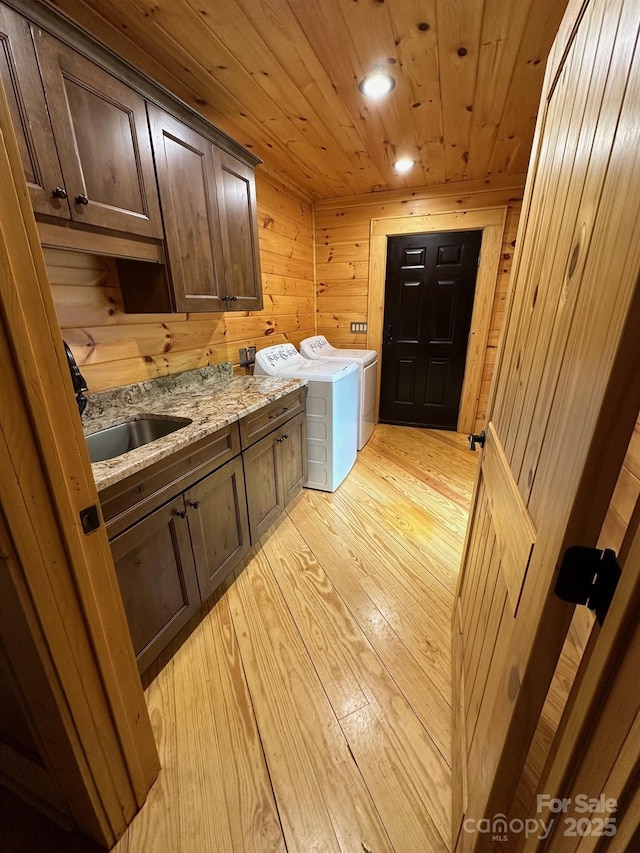 clothes washing area with sink, wood walls, cabinets, wooden ceiling, and washer and clothes dryer