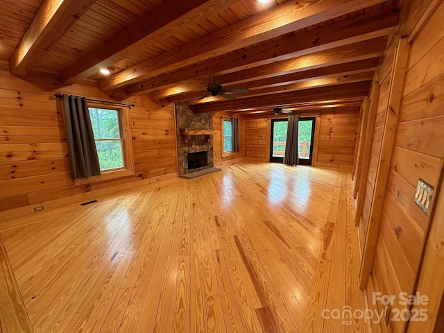 unfurnished living room featuring ceiling fan, a fireplace, wooden walls, and beamed ceiling