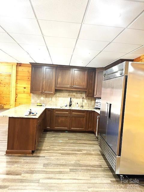 kitchen featuring stainless steel built in refrigerator, a drop ceiling, light hardwood / wood-style floors, and kitchen peninsula