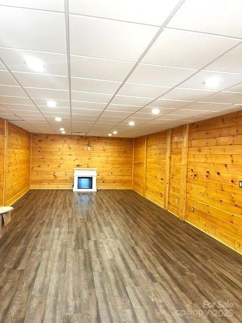 basement featuring a drop ceiling, hardwood / wood-style floors, and wooden walls