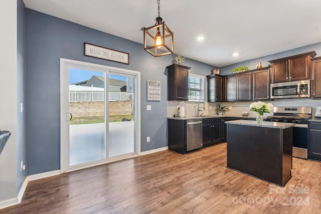 kitchen with tasteful backsplash, light hardwood / wood-style flooring, decorative light fixtures, appliances with stainless steel finishes, and a center island