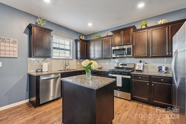 kitchen with light stone counters, a center island, sink, light hardwood / wood-style flooring, and appliances with stainless steel finishes