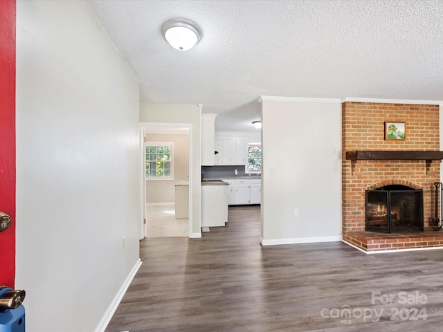 living room with dark wood-type flooring, a textured ceiling, ornamental molding, and a fireplace