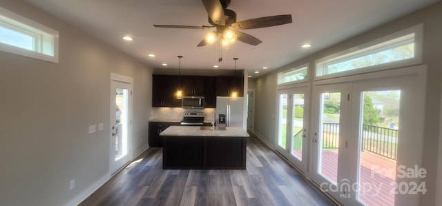 kitchen featuring appliances with stainless steel finishes, dark wood-type flooring, light stone counters, backsplash, and a center island with sink