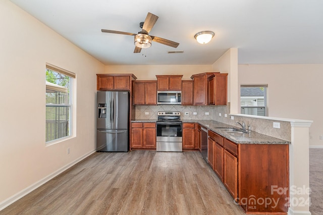 kitchen with kitchen peninsula, appliances with stainless steel finishes, decorative backsplash, light wood-type flooring, and sink