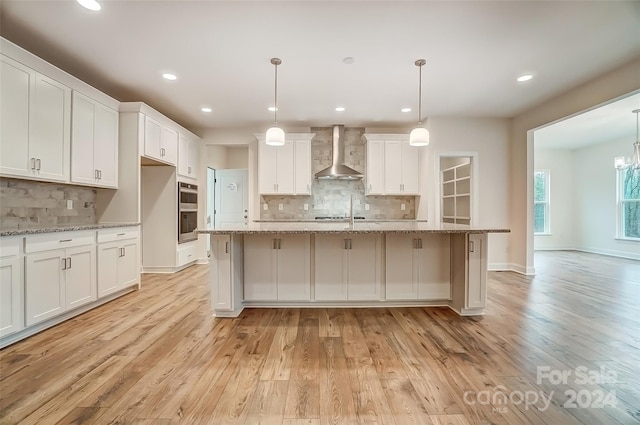 kitchen with light wood-type flooring, wall chimney exhaust hood, and white cabinets