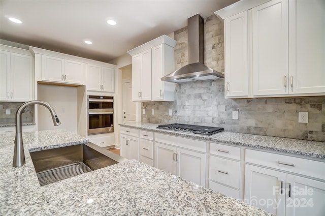 kitchen featuring white cabinetry, wall chimney range hood, appliances with stainless steel finishes, and tasteful backsplash