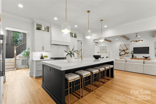 kitchen featuring a center island with sink, a kitchen bar, light wood-type flooring, white cabinets, and pendant lighting