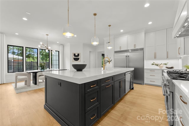 kitchen featuring light wood-type flooring, pendant lighting, premium range hood, high end appliances, and white cabinetry