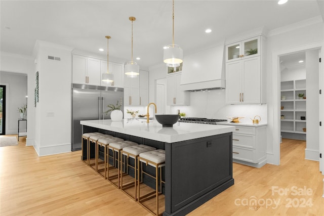 kitchen featuring stainless steel appliances, light wood-type flooring, an island with sink, and premium range hood