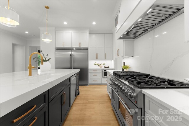 4142 Pineview Rd, Charlotte, NC 28211 - kitchen with high end appliances, wall chimney exhaust hood, white cabinets, light wood-style flooring, and pendant lighting