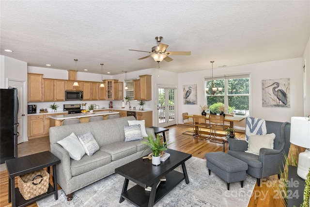 living room with light wood-type flooring, a textured ceiling, ceiling fan with notable chandelier, and sink