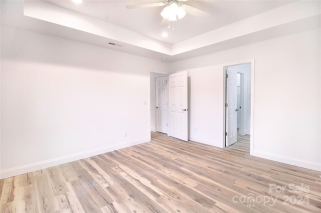 unfurnished bedroom with ceiling fan, light hardwood / wood-style floors, and a tray ceiling