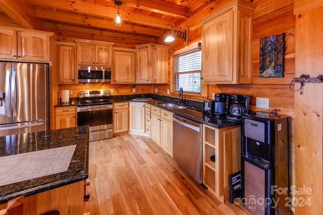 kitchen with appliances with stainless steel finishes, light hardwood / wood-style flooring, beam ceiling, dark stone countertops, and sink