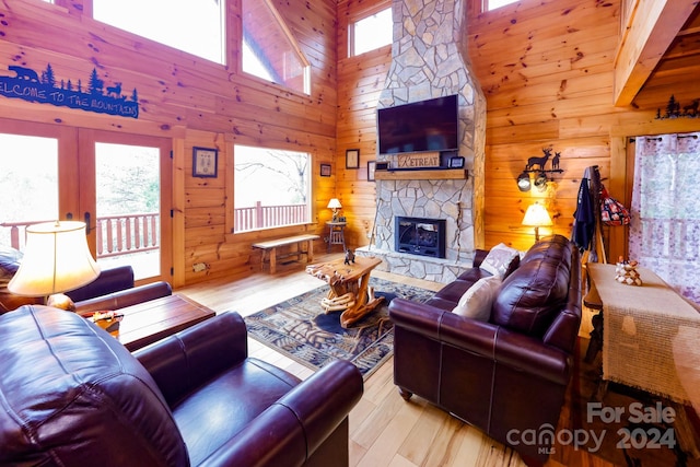 living room with high vaulted ceiling, light hardwood / wood-style flooring, wood walls, and a stone fireplace