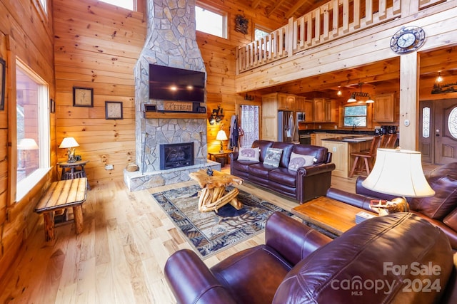 living room with a fireplace, high vaulted ceiling, light hardwood / wood-style floors, wood ceiling, and wooden walls