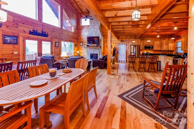 dining room featuring ceiling fan, a fireplace, light hardwood / wood-style floors, beam ceiling, and wooden walls