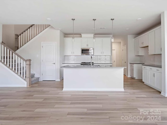 kitchen with light wood-type flooring, white cabinets, decorative light fixtures, and a kitchen island with sink