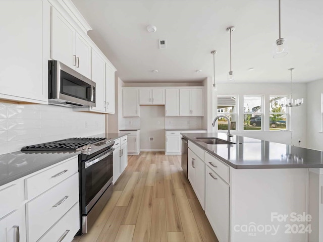 kitchen featuring light wood-type flooring, appliances with stainless steel finishes, pendant lighting, sink, and an island with sink