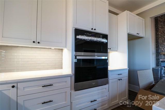 kitchen with light stone countertops, white cabinetry, double wall oven, and backsplash