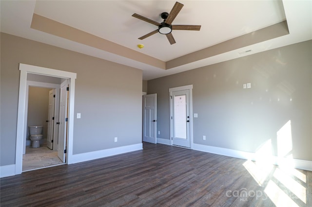 unfurnished bedroom with connected bathroom, dark hardwood / wood-style floors, and a raised ceiling