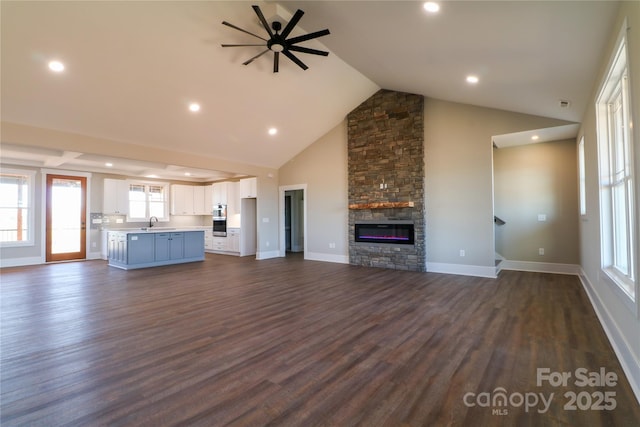 unfurnished living room featuring a stone fireplace, dark wood-type flooring, high vaulted ceiling, and a wealth of natural light