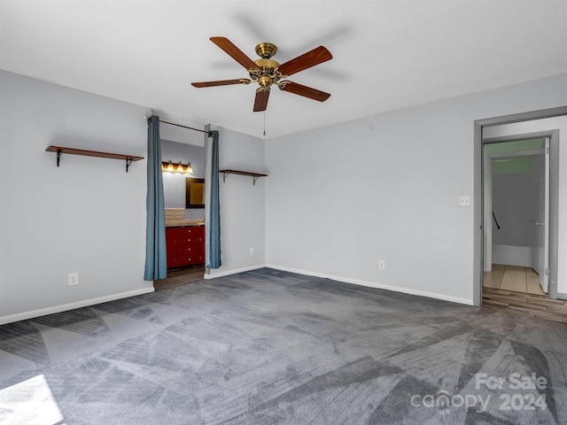 unfurnished bedroom featuring ceiling fan, dark carpet, and ensuite bath