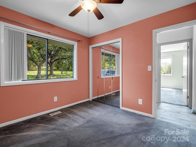 unfurnished bedroom with a closet, multiple windows, ceiling fan, and dark colored carpet