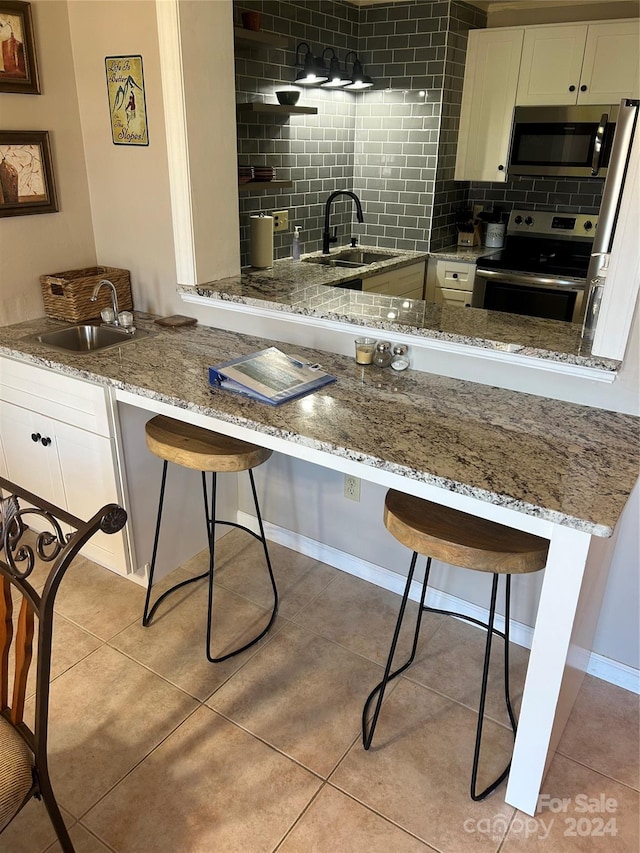 kitchen featuring light stone countertops, backsplash, stainless steel appliances, white cabinets, and sink