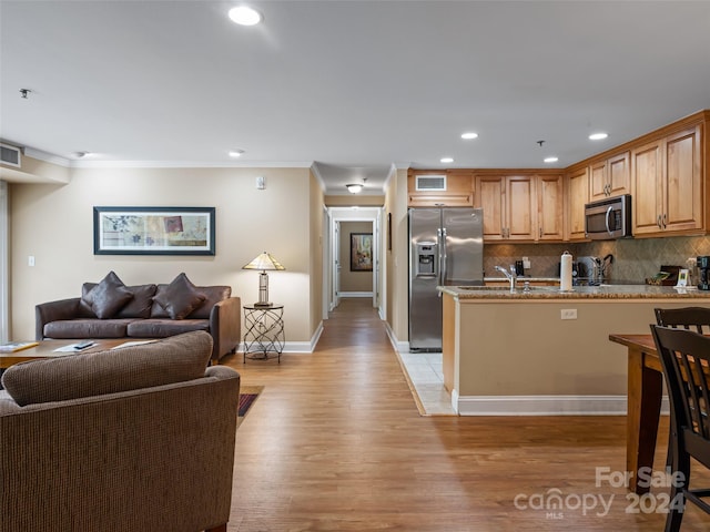 kitchen featuring light stone countertops, backsplash, appliances with stainless steel finishes, a kitchen bar, and light hardwood / wood-style floors